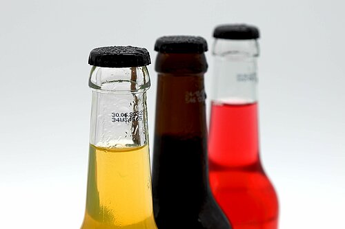 Mehrere Glasflaschen mit unterschiedlichen Getränken und aufgedruckter Kennzeichnung