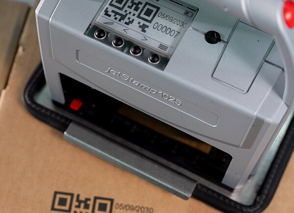 Mobiler Handdrucker REINER jetStamp 1025 druckt QR-Code und Recyclingsymbol auf Karton.